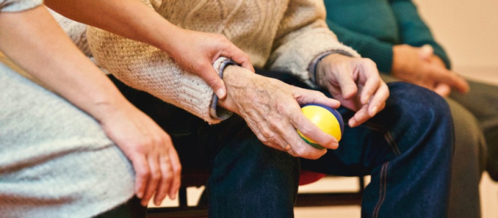 Mão ajuda um homem velho que recebe Complemento Solidário para idosos e segura uma bola amarela.