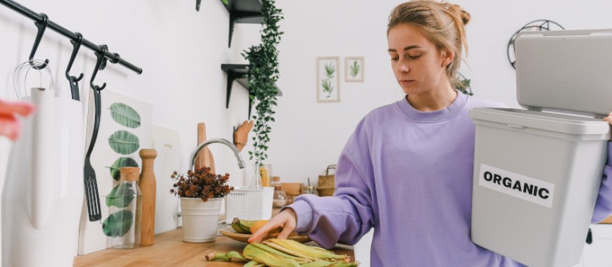 Mulher de camisola lilás, na cozinha, a separar lixo orgânico e a pensar como reduzir o lixo doméstico.