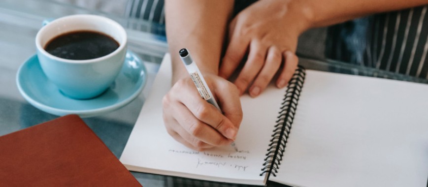 Mãos de pessoa a escrever à mão com uma caneta num caderno.