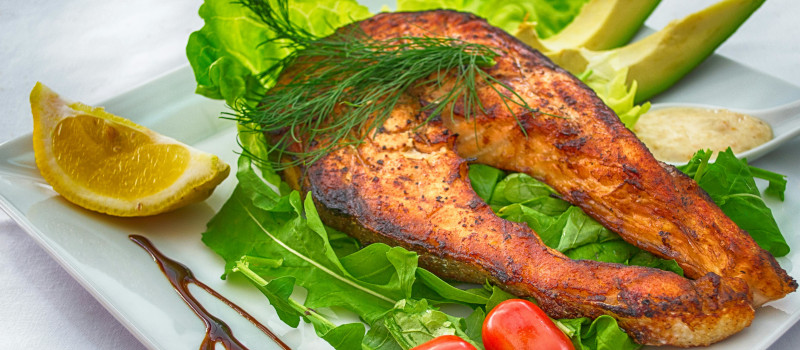 Posta de salmão grelhado no prato com verduras ao lado num exemplo de proteínas saudáveis.