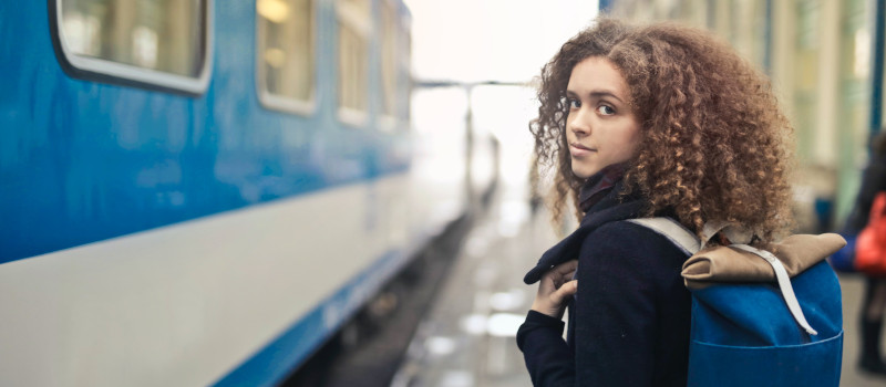 Mulher jovem morena, de cabelos encaracolados, com casaco preto e mochila azul às costas prestes a usar o passe Navegante metropolitano no metro.