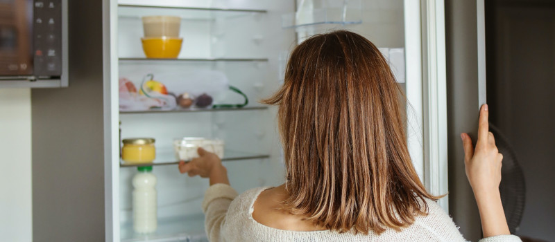 Mulher de costas a tirar produto do interior de uma geladeira depois de limpar frigorifico com vinagre.