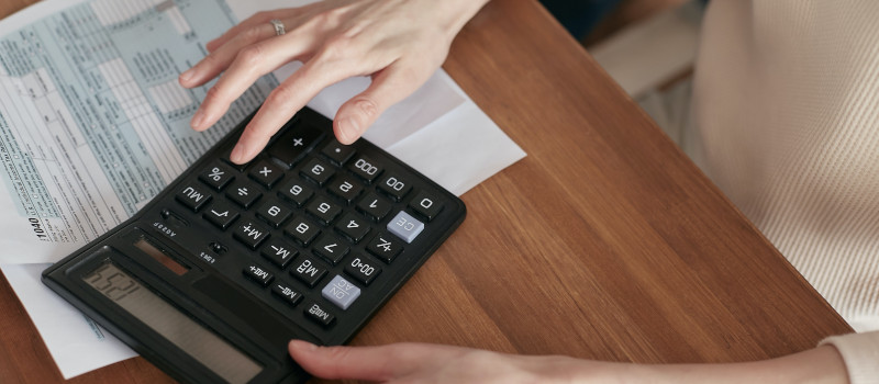 Mãos de mulher tocam em calculadora preta sobre a mesa e formulário sobre o IAS, ou Indexante dos Apoios Sociais.