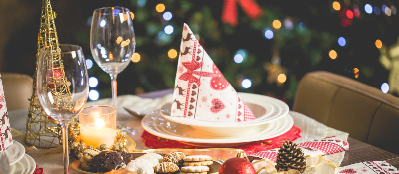 Pormenor da mesa da ceia de Natal, com um guardanapo com enfeites a vermelho em forma de pirâmide no prato.