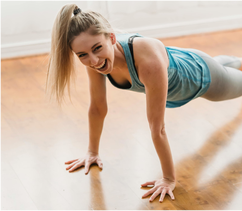 Mulher loura, de cabelo apanhado, em pose de Yoga do riso, com camisola azul cavada a fazer exercícios de terapia do riso.