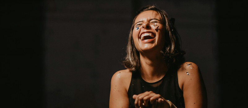 Mulher de cabelo pelos ombros e camisola preta a rir à gargalhada durante terapia do riso.