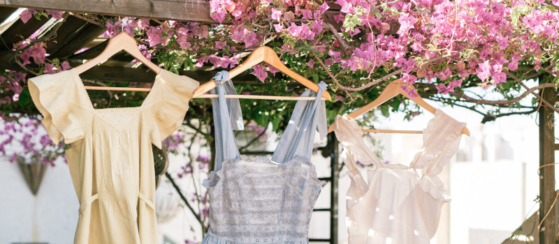 Três vestidos pendurados em cabides, com flores cor-de-rosa em cima, para mostrar como estender a roupa.