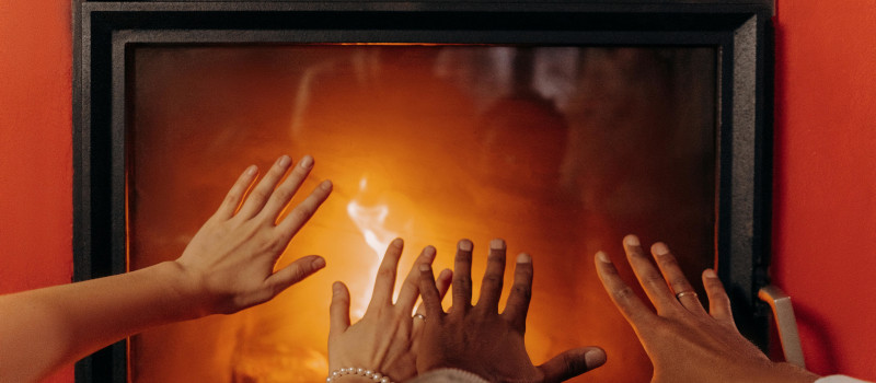 Várias mãos estendidas, a aquecerem-se numa lareira acesa, depois de terem visto como limpar o vidro da lareira.