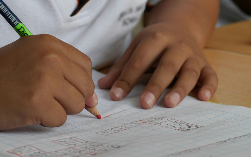 Mãos de menino sobre um caderno com uma mão a escrever com a preensão do lápis em pinça.