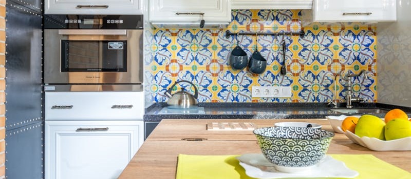 cozinha de azulejos coloridos, equipada com microondas embutido em armário, chaleira e outros utensílios no balcão e nas paredes