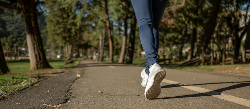 Pernas de mulher com leggings e ténis a correr num parque com árvores.